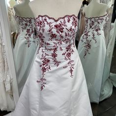 a white dress with red appliques is on display in front of other dresses