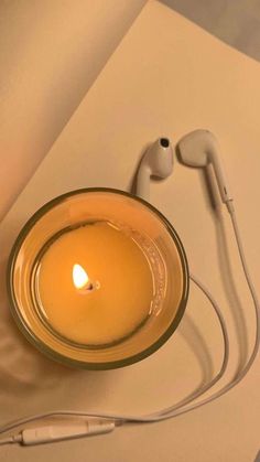 a glass bowl with a candle and headphones on it sitting next to a sheet of paper