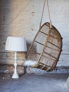 a rattan hanging chair next to a lamp on the floor in front of a brick wall