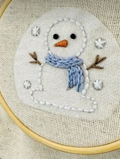 a close up of a snowman embroidered on a piece of cloth in a hoop