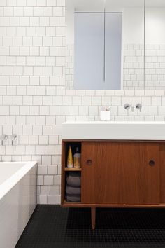 a bathroom with a sink, mirror and bathtub next to a white tiled wall