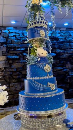 a three tiered blue cake decorated with flowers and a teddy bear sitting on top