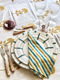 the table is set with silverware and striped napkins, gold - plated utensils