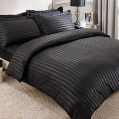 a bed with black comforter and pillows in a room next to a lamp on a table