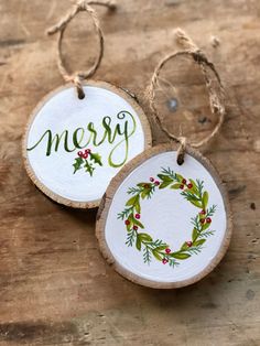 two wooden christmas ornaments with the word merry painted on them, hanging from twine strings