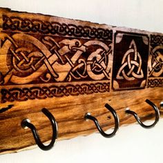 a wooden coat rack with metal hooks and celtic designs on the front, hanging from a white wall