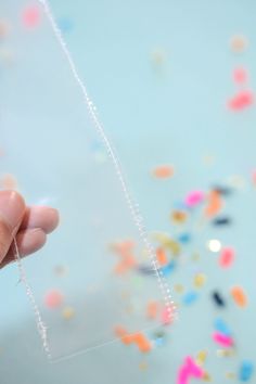 a hand holding a piece of clear plastic with sprinkles on the background