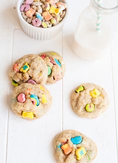 three cookies with m & m on them next to a bowl of cereal and a glass of milk