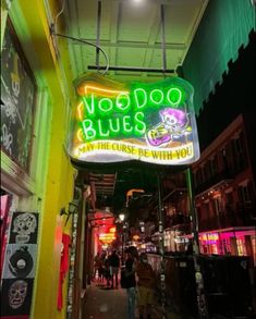 the neon sign for voodoo blues is lit up in green and yellow colors, along with people walking down the sidewalk