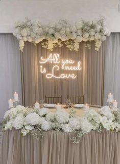 a table topped with white flowers and candles next to a sign that says all you need is love