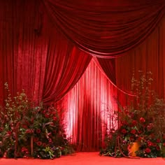 a red stage set up with flowers and greenery in front of a curtained area