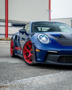 a blue sports car with red rims parked in front of a large warehouse building