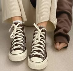 a person wearing brown and white sneakers with their legs crossed on the floor next to each other