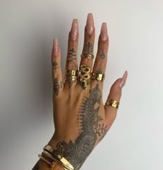 a woman's hand with tattoos and gold rings on her left wrist, holding onto a white wall