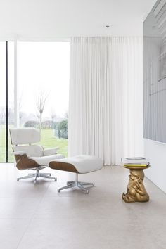 a modern living room with white curtains and an eames chair in the foreground