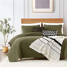 a bed with green bedspread and black and white pillows on top of it