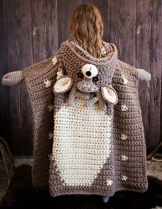 a woman is wearing a crocheted bear ponchy and standing in front of a wooden wall