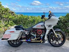 a white motorcycle parked on the side of a road next to the ocean and trees