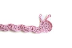 a pink crocheted object is shown on a white surface and it looks like a worm