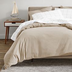 an unmade bed with beige sheets and pillows on it in a room next to a wooden table