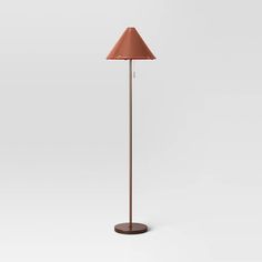 a floor lamp with a brown shade on the base and a white wall behind it