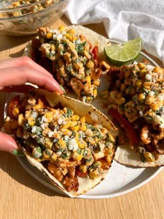 a plate with three tacos on it and a hand reaching for the tortilla