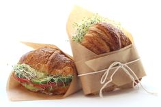 two croissant sandwiches wrapped in brown paper