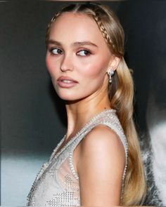 a woman with long blonde hair in a braid wearing a silver dress and diamond earrings