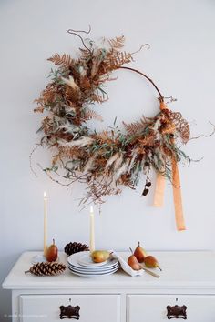 a white dresser topped with a wreath and plates filled with fruit on top of it