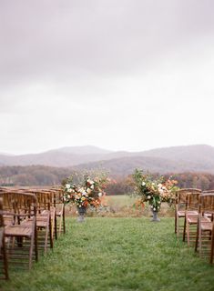 an outdoor ceremony setup with wooden chairs and floral centerpieces on the grass in front of mountains