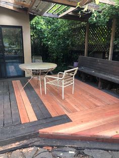 a table and chairs on a wooden deck in front of a patio with a bench