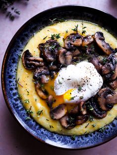 a blue bowl filled with mashed potatoes and mushrooms topped with an egg on top