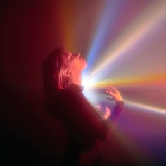 a woman standing in front of a colorful light with her hands on the side of her face