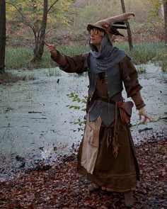 a man dressed in costume standing next to a body of water with trees and leaves around him