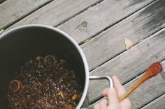 a person holding a wooden spoon over a pot filled with food on top of a wooden table