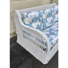 a wicker couch with blue and white flowers on it sitting in front of a garage door