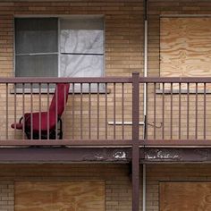 a red chair sitting on top of a balcony next to a building with boarded up windows