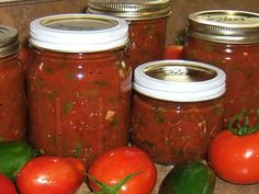 several jars filled with different kinds of food on a counter next to tomatoes and peppers