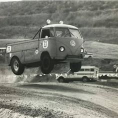 an old vw bus is flying through the air in front of other cars on a dirt road