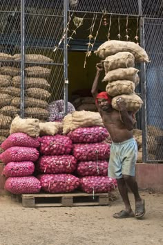 a man carrying bags on his head in front of a pile of onions and potatoes