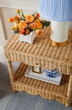 a wicker table with a blue and white vase on it next to a lamp