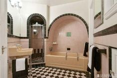 a bathroom with black and white checkered flooring, pink bathtub and sink