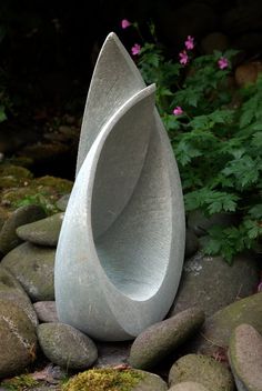 a large white vase sitting on top of a pile of rocks next to some flowers