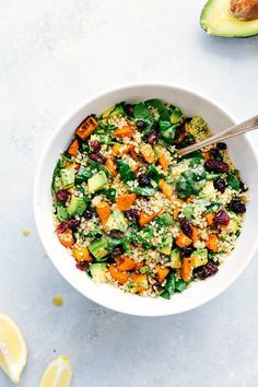 a white bowl filled with salad next to sliced avocado and lemon wedges