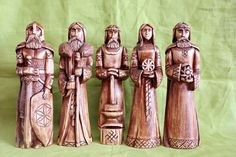 four wooden figurines are lined up on a green clothed surface, one is wearing a crown and the other has a cross