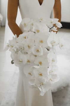 a bride holding a bouquet of white orchids in her wedding dress and looking at the camera