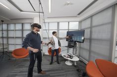 two men standing in an office talking to each other while one man is holding a video game controller