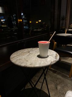 a cup sitting on top of a marble table next to a black chair and window