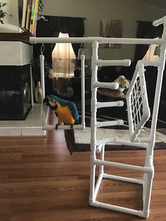 a toy parrot sitting on top of a wooden floor next to a white swing frame