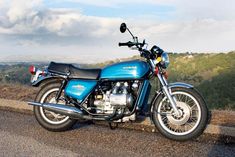 a blue motorcycle parked on the side of a road next to a hill and trees